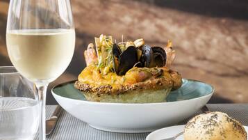 A dessert plate with a pastry topped with seafood and vegetables, a glass of white wine, and a small plate with butter and red peppercorns.