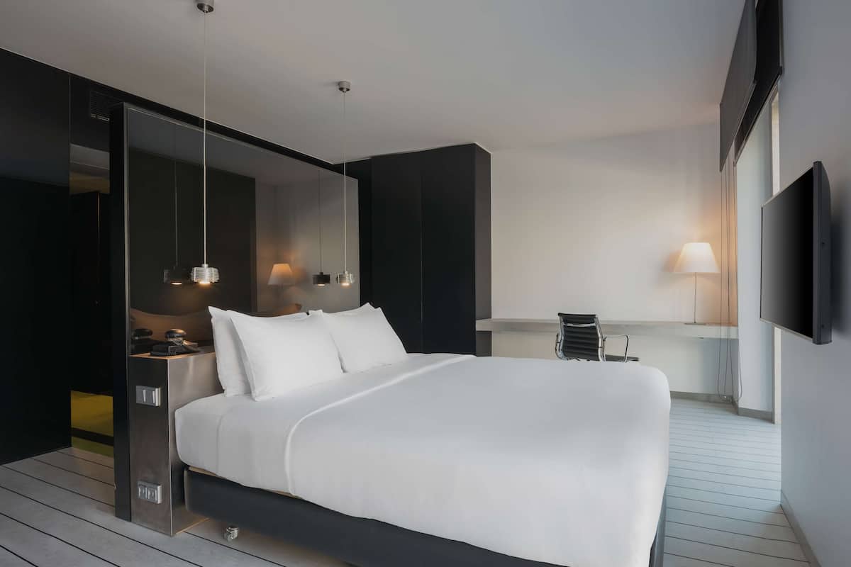 Una habitación de hotel moderna con una cama grande, un escritorio, una silla y un televisor montado en la pared.