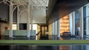 Un vestíbulo moderno con un piso negro elegante, columnas blancas estructurales y una gran pared de vidrio con chimenea.