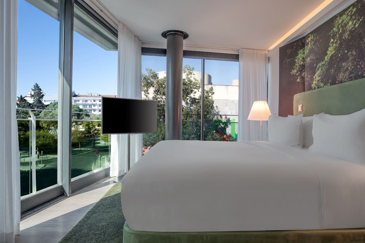 Una habitación de hotel moderna con una cama grande, televisión de pantalla plana y vistas a la ciudad a través de ventanas de gran altura.