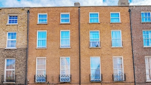 A row of three-story brick townhouses with white-framed windows, a central entrance with a door, and a small balcony on the second floor. - Iveagh Lodge (Dublin)