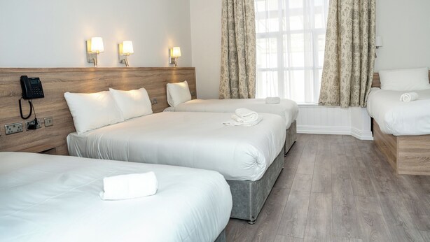 A hotel room with three beds, a bedside telephone, and two wall-mounted lamps. - Iveagh Lodge (Dublin)