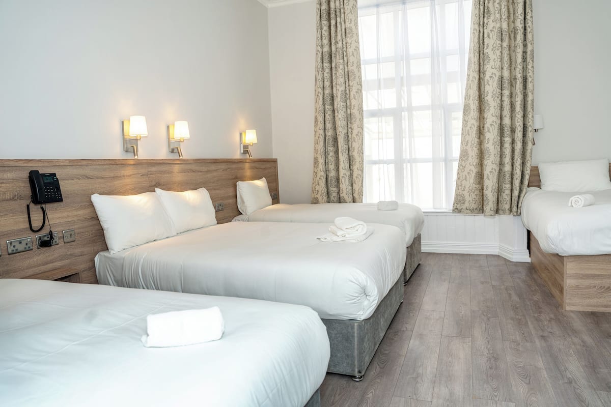 A hotel room with three beds, a bedside telephone, and two wall-mounted lamps.