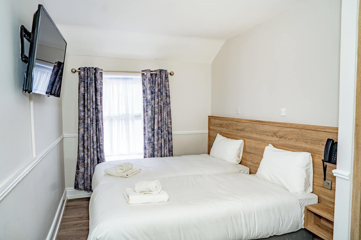 A hotel room with a large bed, a TV mounted on the wall, and a telephone on the nightstand.