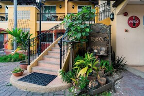 A staircase leading to a building entrance with a Coca-Cola sign, surrounded by potted plants and a metal grate. - Crown Regency Residences Davao (Davao)