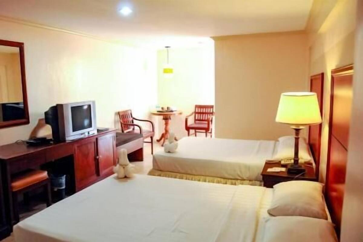 A hotel room with two beds, a desk with a television, a chair, a lamp, and a small table.