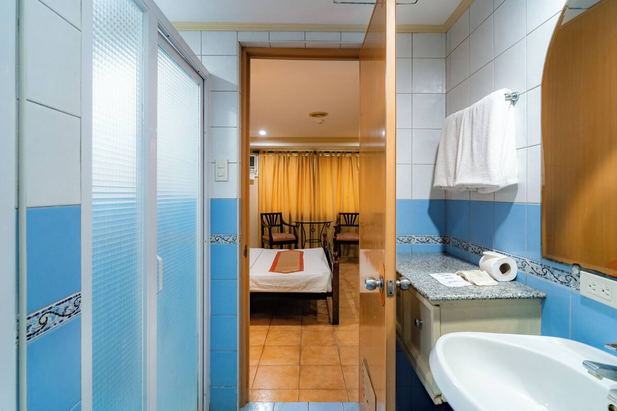 A hotel room with a bed, a bathroom with a sink and mirror, and a dining area with chairs and a table.