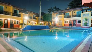 A swimming pool surrounded by buildings with balconies, a palm tree, and a staircase leading to the upper floors.