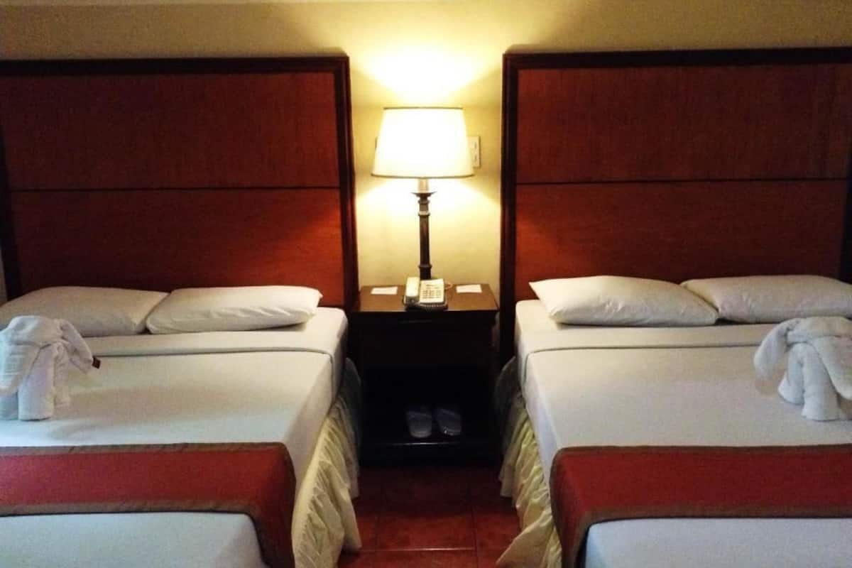 A hotel room with two beds, a nightstand with a lamp, and a pair of slippers.