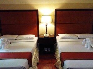 Une chambre d’hôtel avec deux lits, une table de chevet avec une lampe et une paire de chaussures sur le sol.
