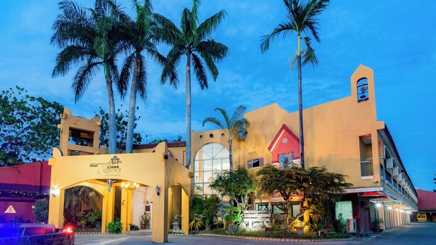 A hotel with a large arched entrance, palm trees, and a red building in the background.