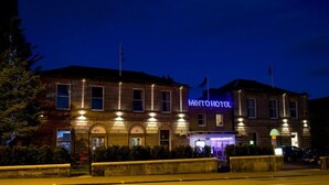 Un hotel amb un cartell de neó ben visible, façana de pedra i entrada ben il·luminada.
