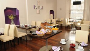 Una zona de menjador amb diverses taules i caires, disposades en una habitació àmplia amb terres de fusta i parets de color crema.