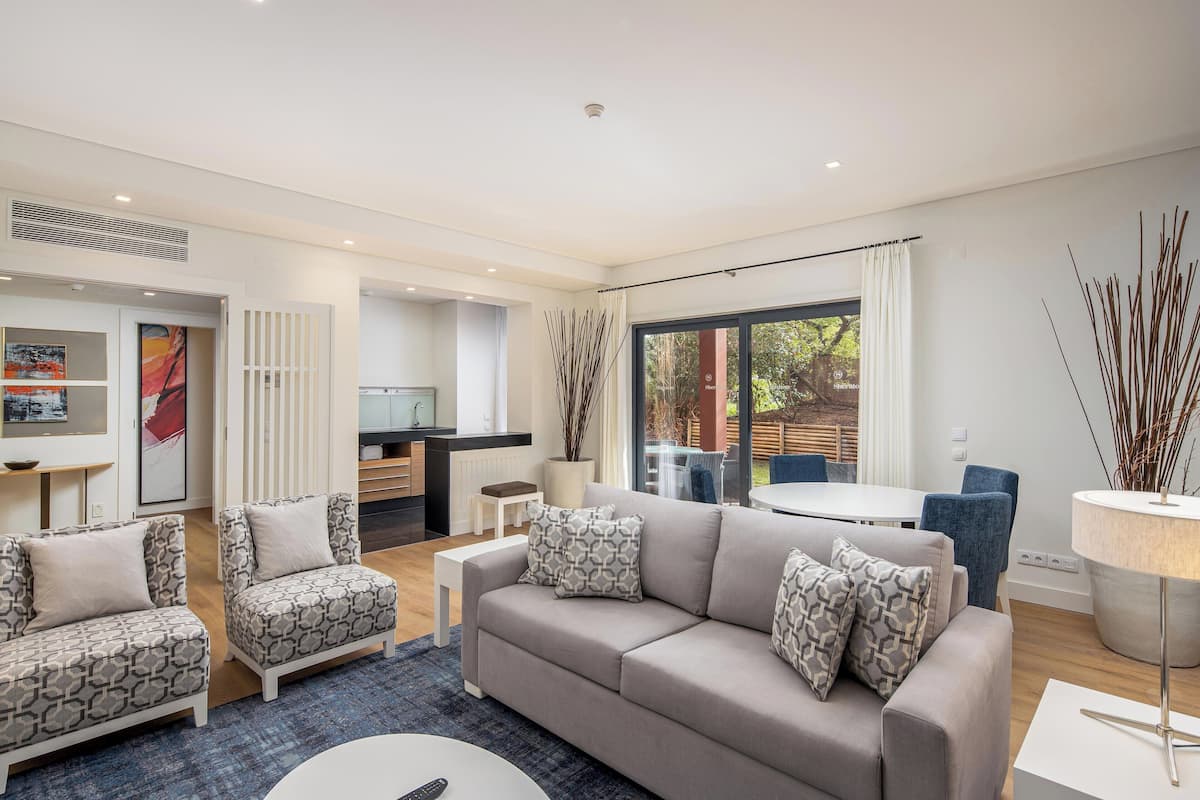 Una sala de estar moderna con un sofá gris, sillones estampados y una zona de comedor con mesa y sillas.