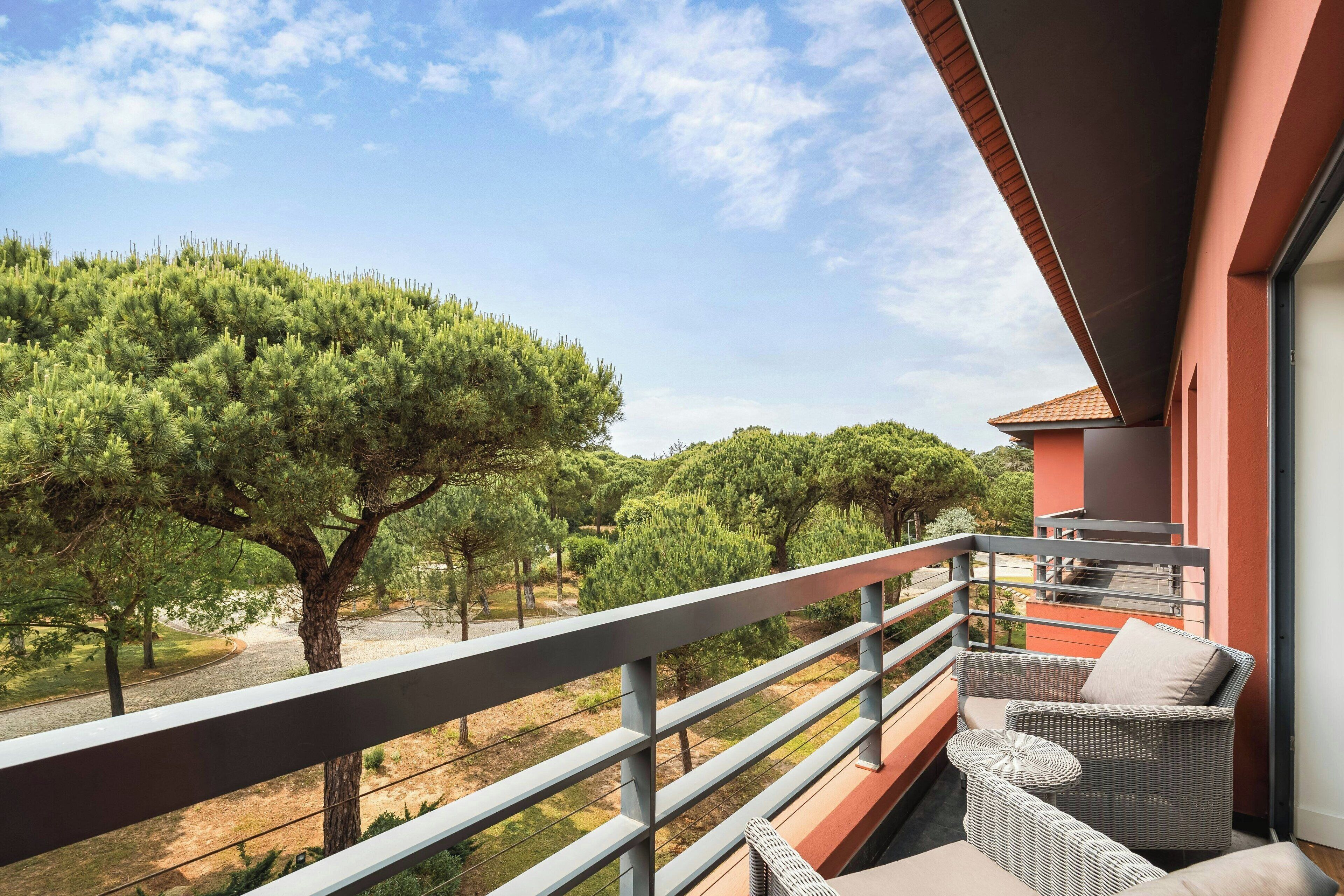 A balcony with wicker furniture, a view of trees, and a clear sky.