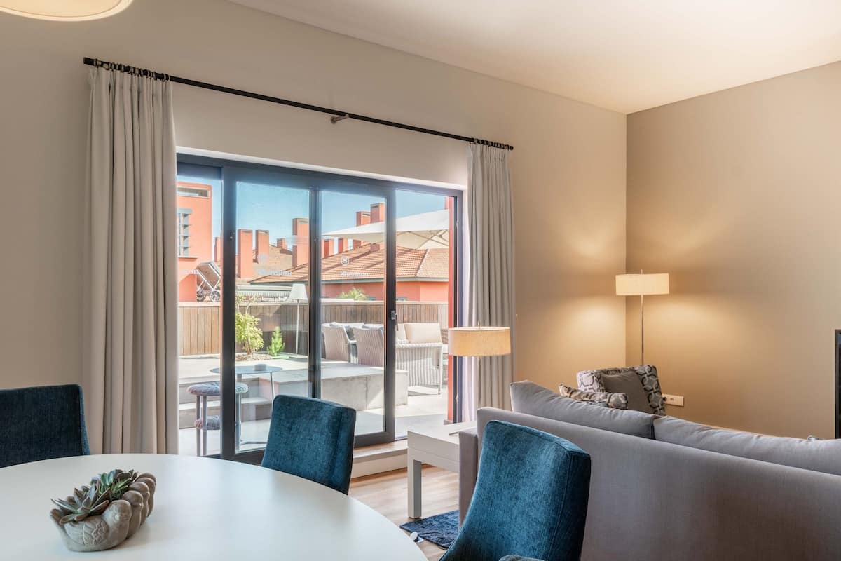 Una sala de estar moderna con un sofá, una mesa de comedor con sillas y un amplio ventanal corredero que da a un patio exterior.