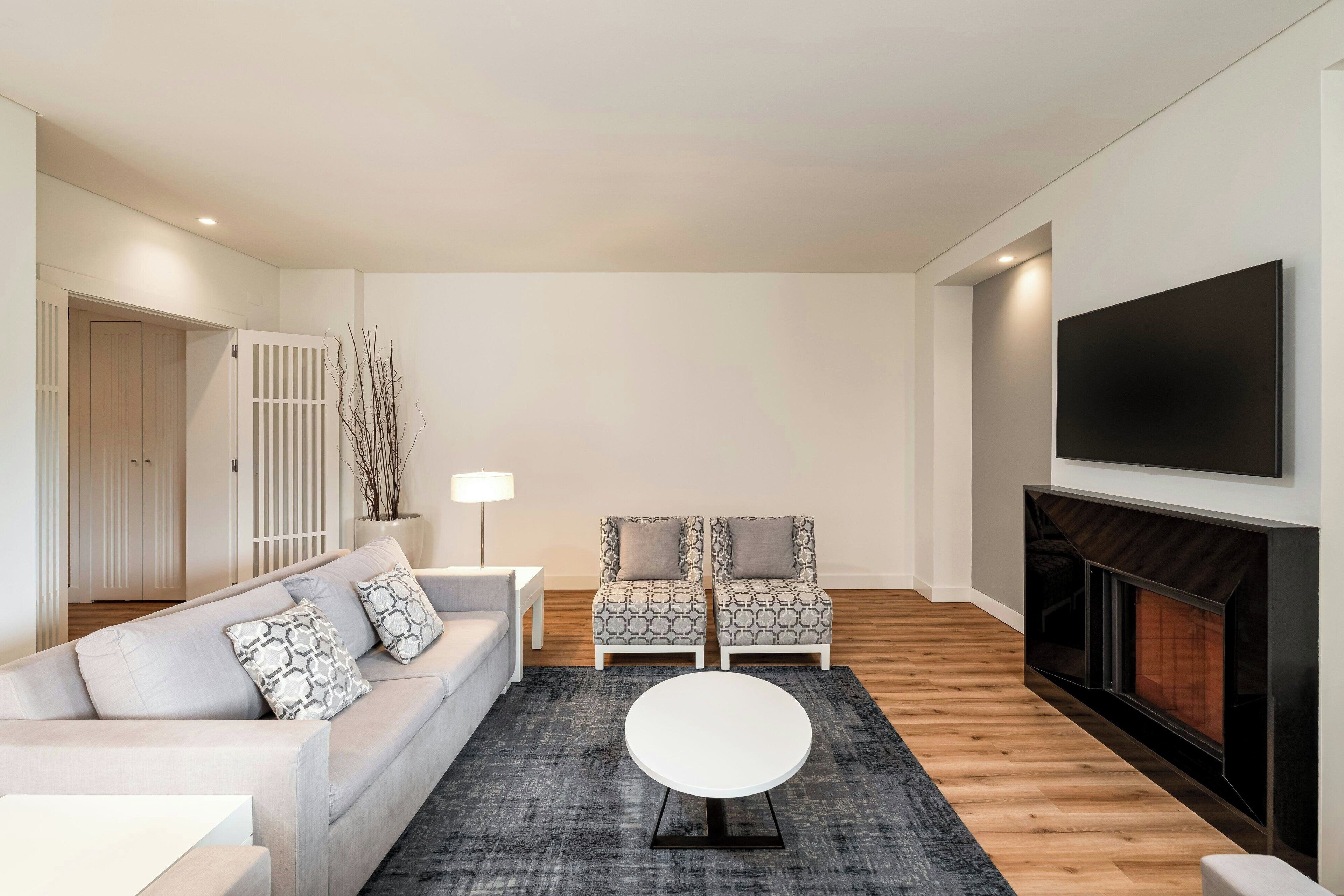 Un salon moderne comprenant un canapé, deux fauteuils à motifs, une table basse ronde, une cheminée et un téléviseur fixé au mur.