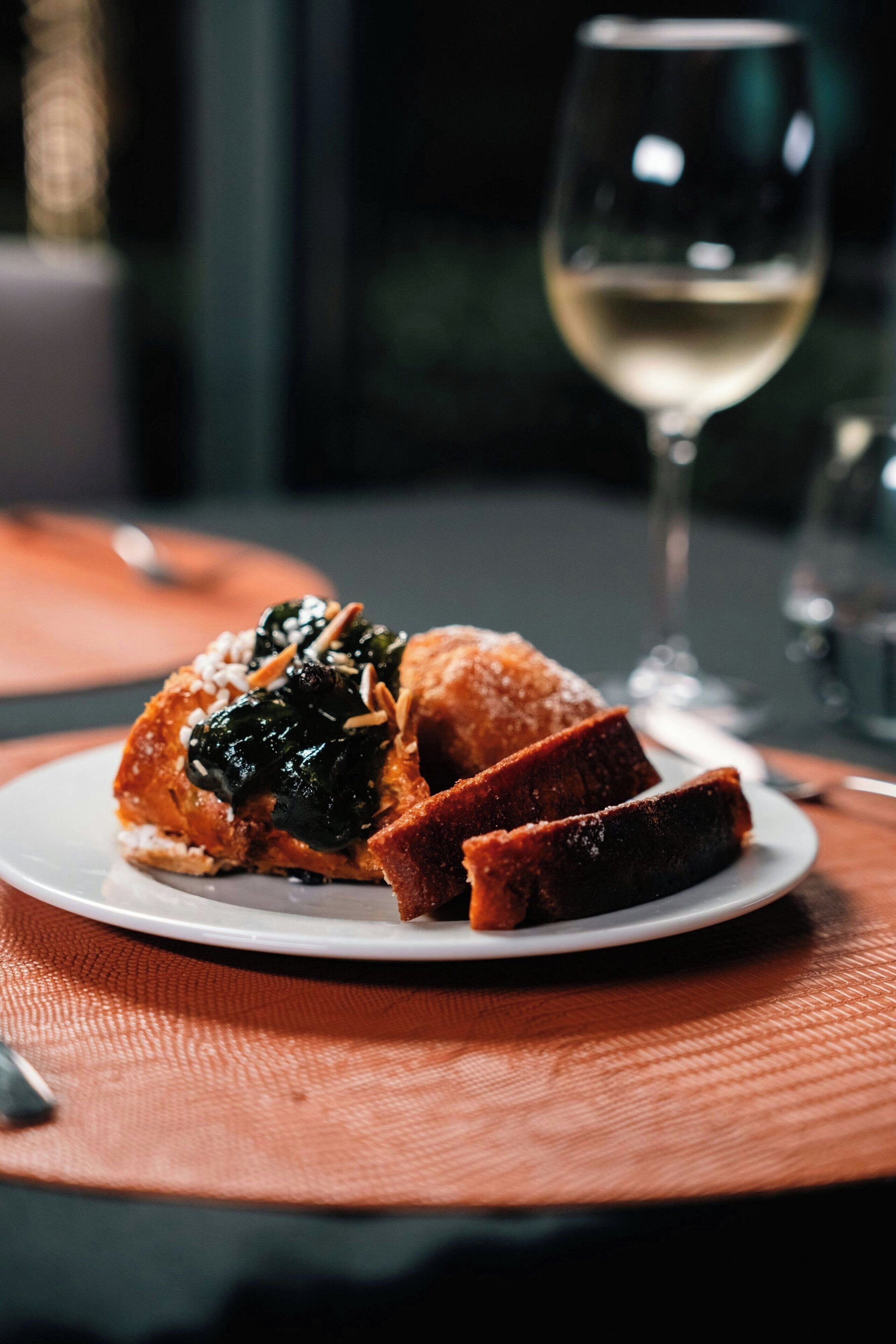 A plate with a dessert and a glass of white wine on a table.