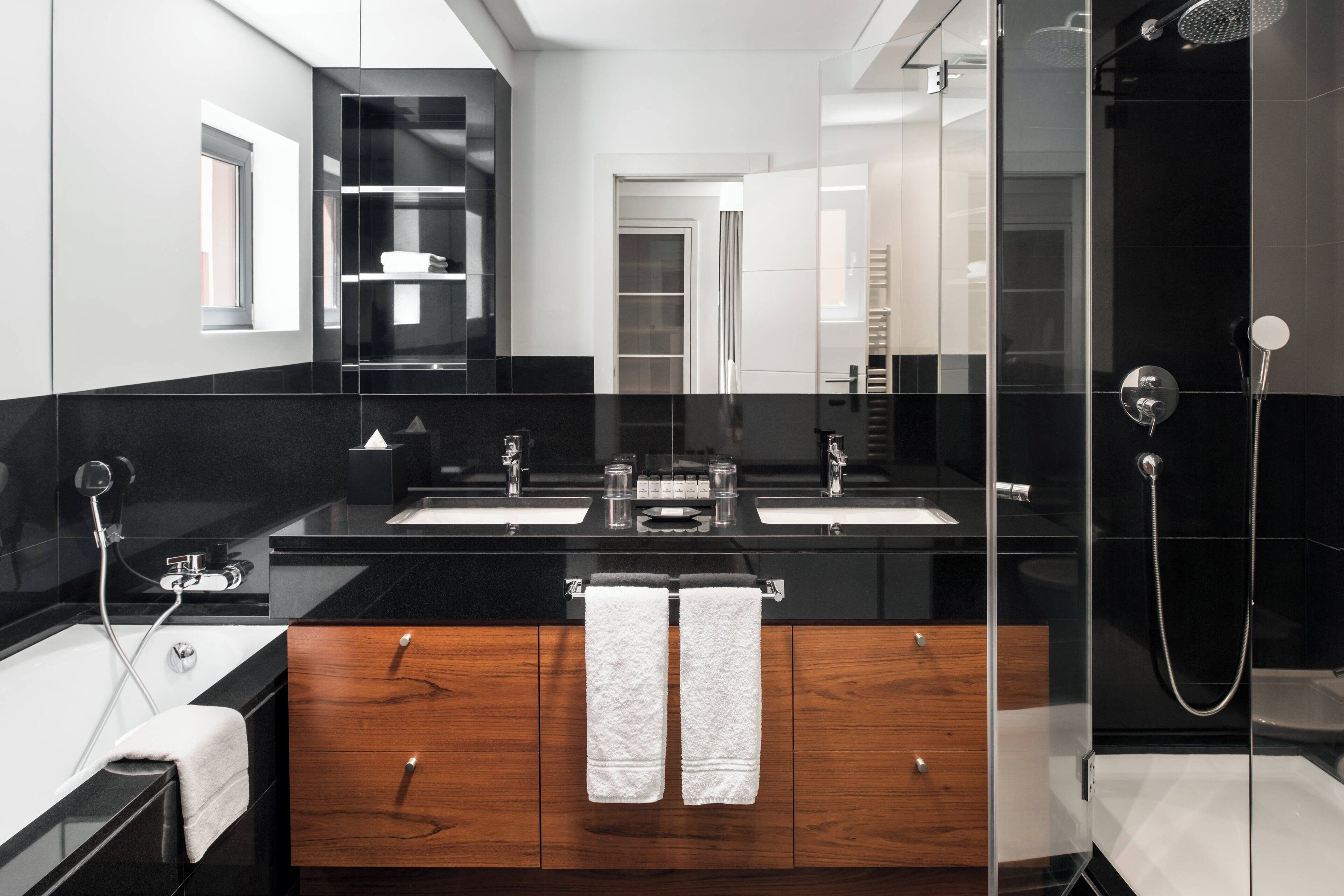 Een moderne badkamer met twee wastafels, een douchecabine met glazen wanden en een badkamermeubel met houten kastjes.