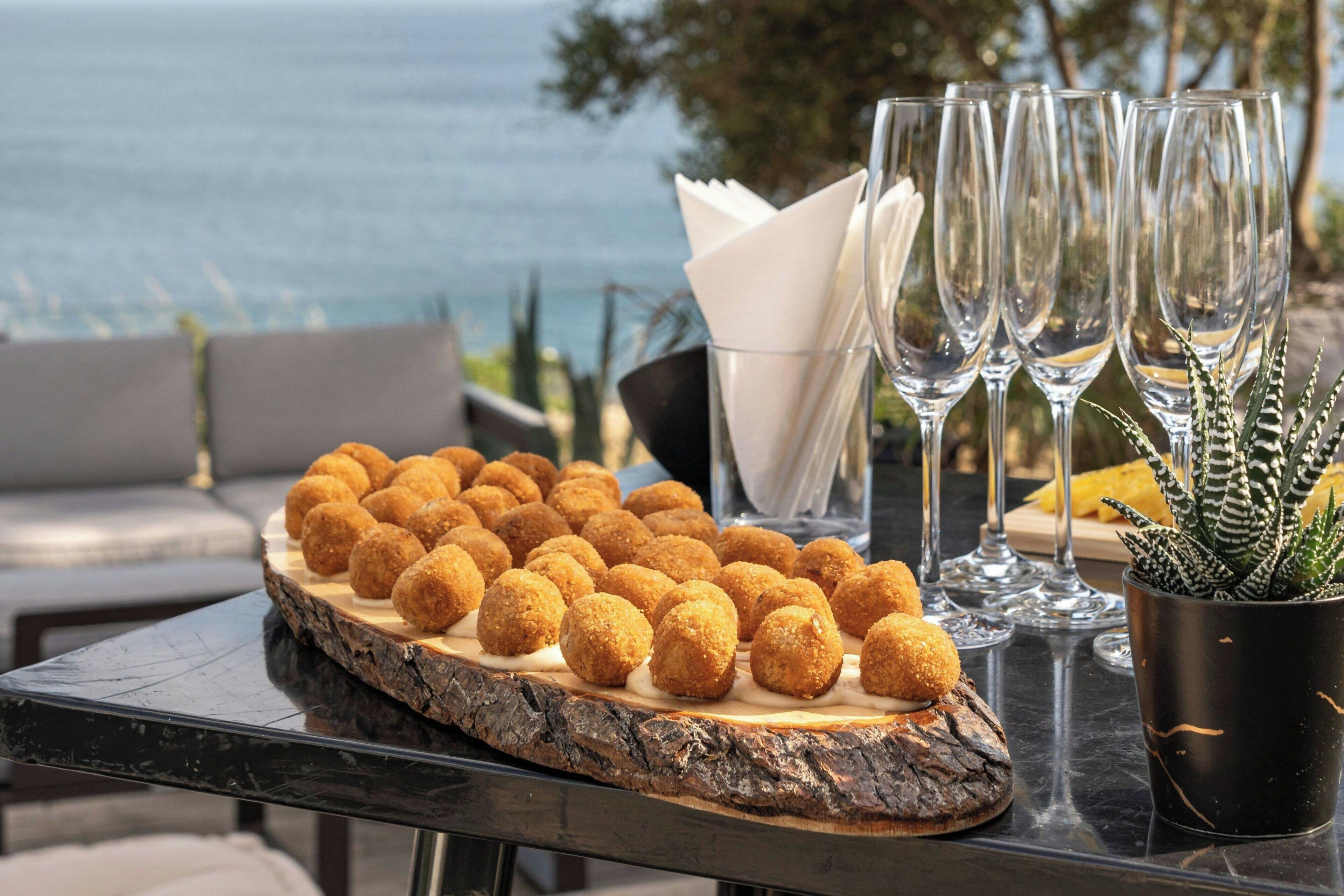 A table with croquettes, wine glasses, and a potted plant.