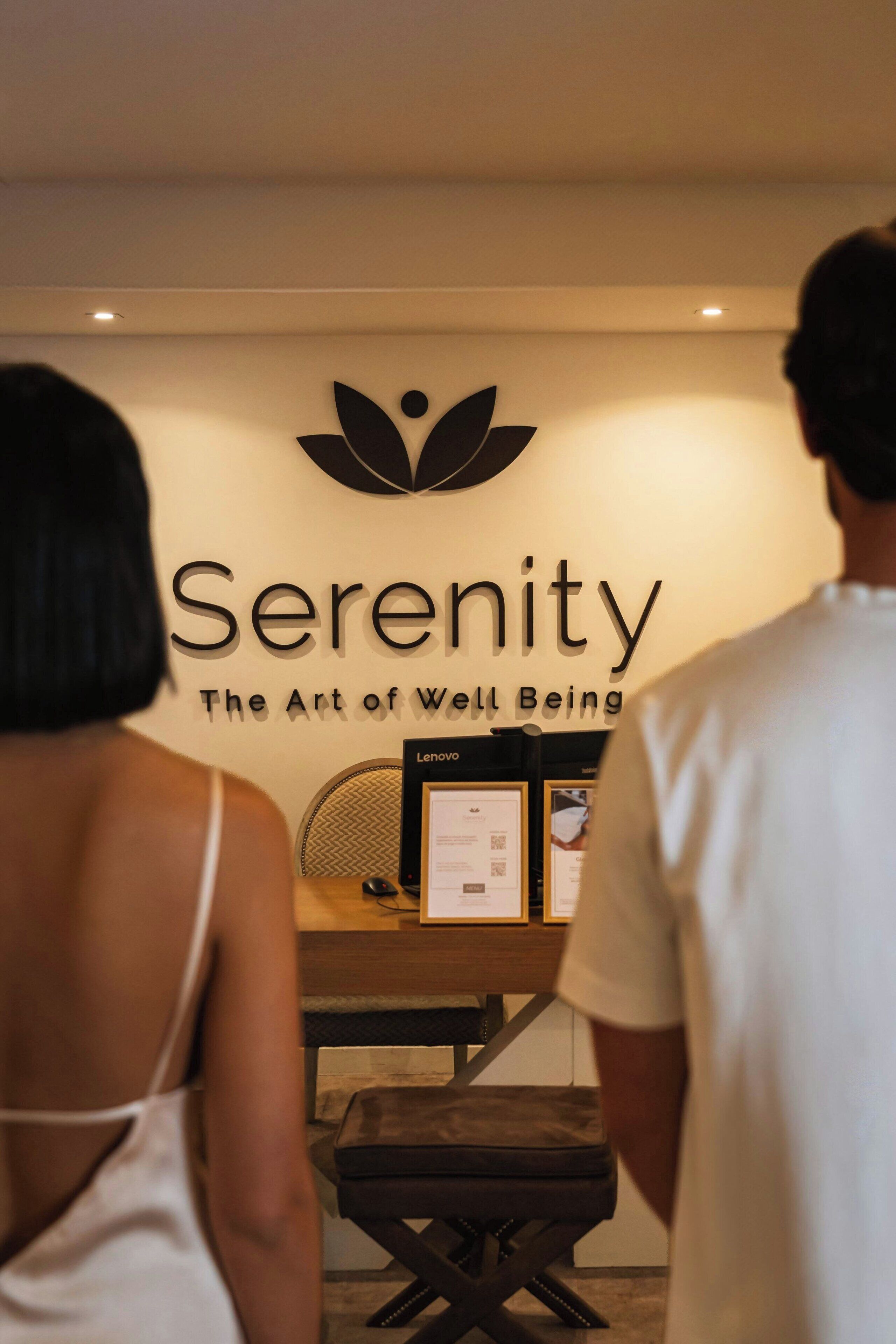 A reception desk with a sign reading "Serenity The Art of Well Being" and a logo above it.
