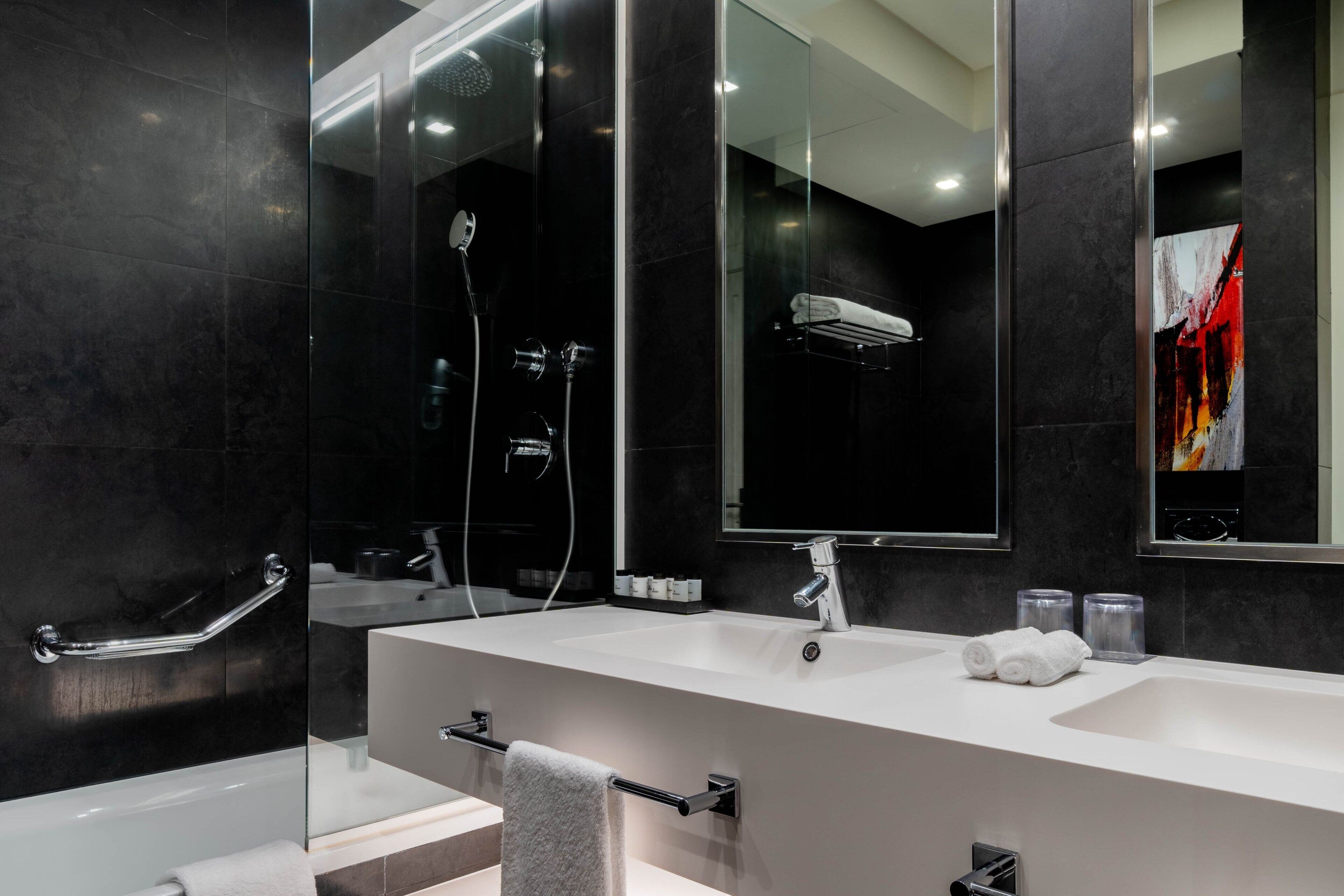 Un baño moderno con un espejo grande, dos lavamanos, una ducha y zona de ducha con mampara de vidrio.