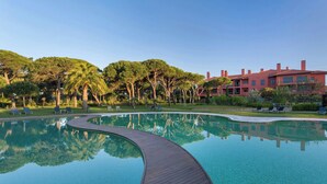 Una piscina con cubierta de madera, rodeada de árboles y un edificio con tejados rojos.