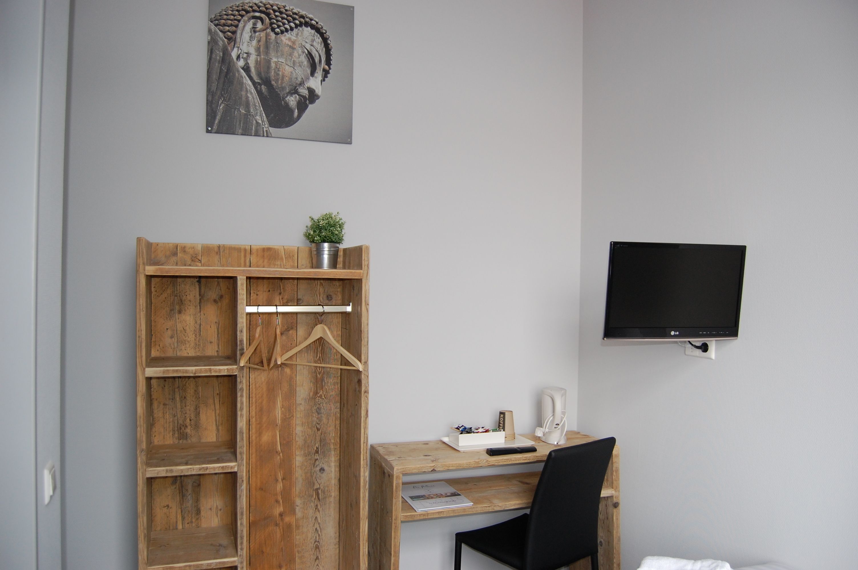 Ein Zimmer mit einem Holzkleiderschrank, einem Schreibtisch mit Stuhl, einem Flachbildfernseher und einem Buddha-Gemälde an der Wand.