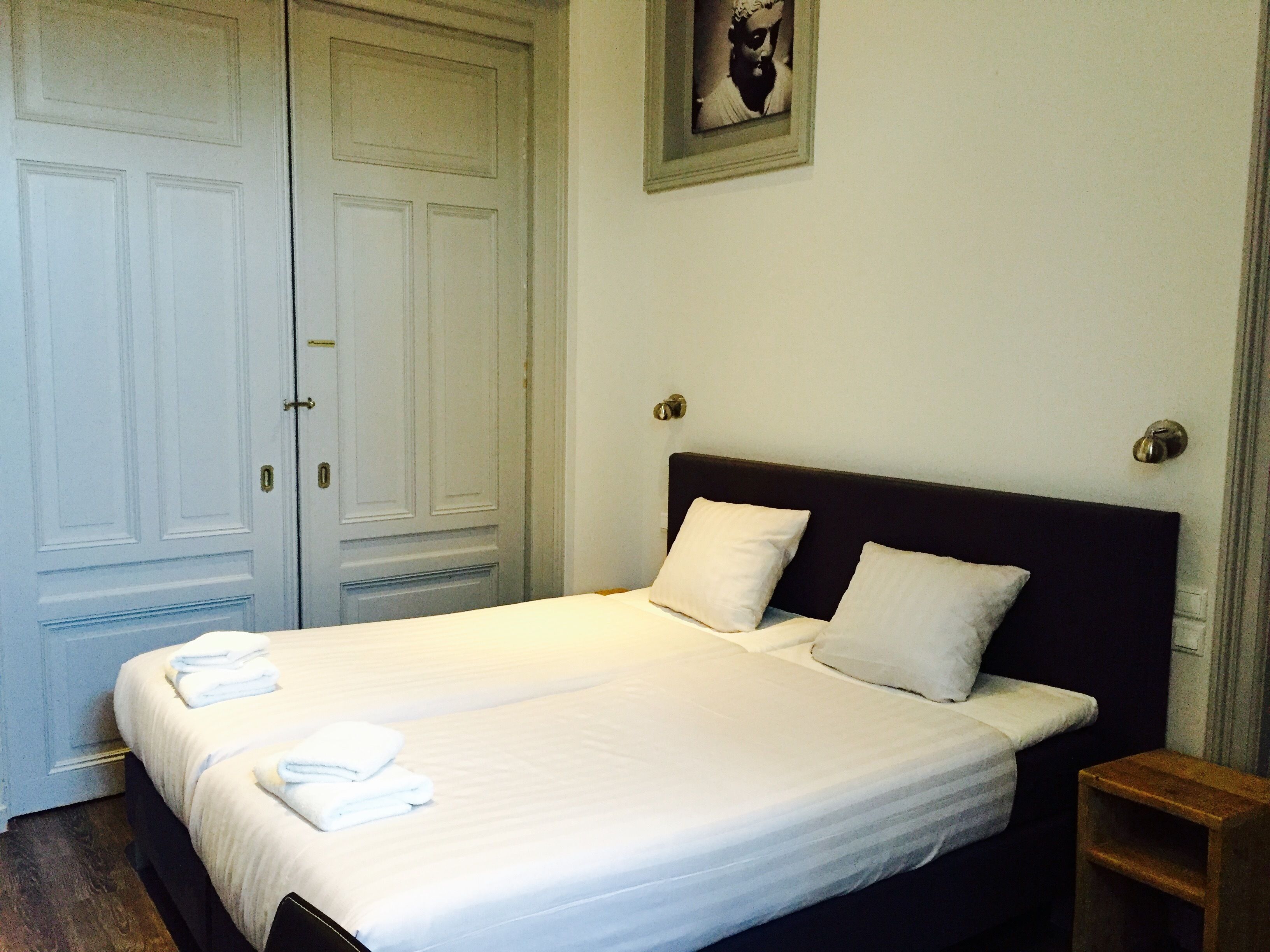 A neatly made bed with white linens and pillows, a wooden nightstand, and a framed picture on the wall.
