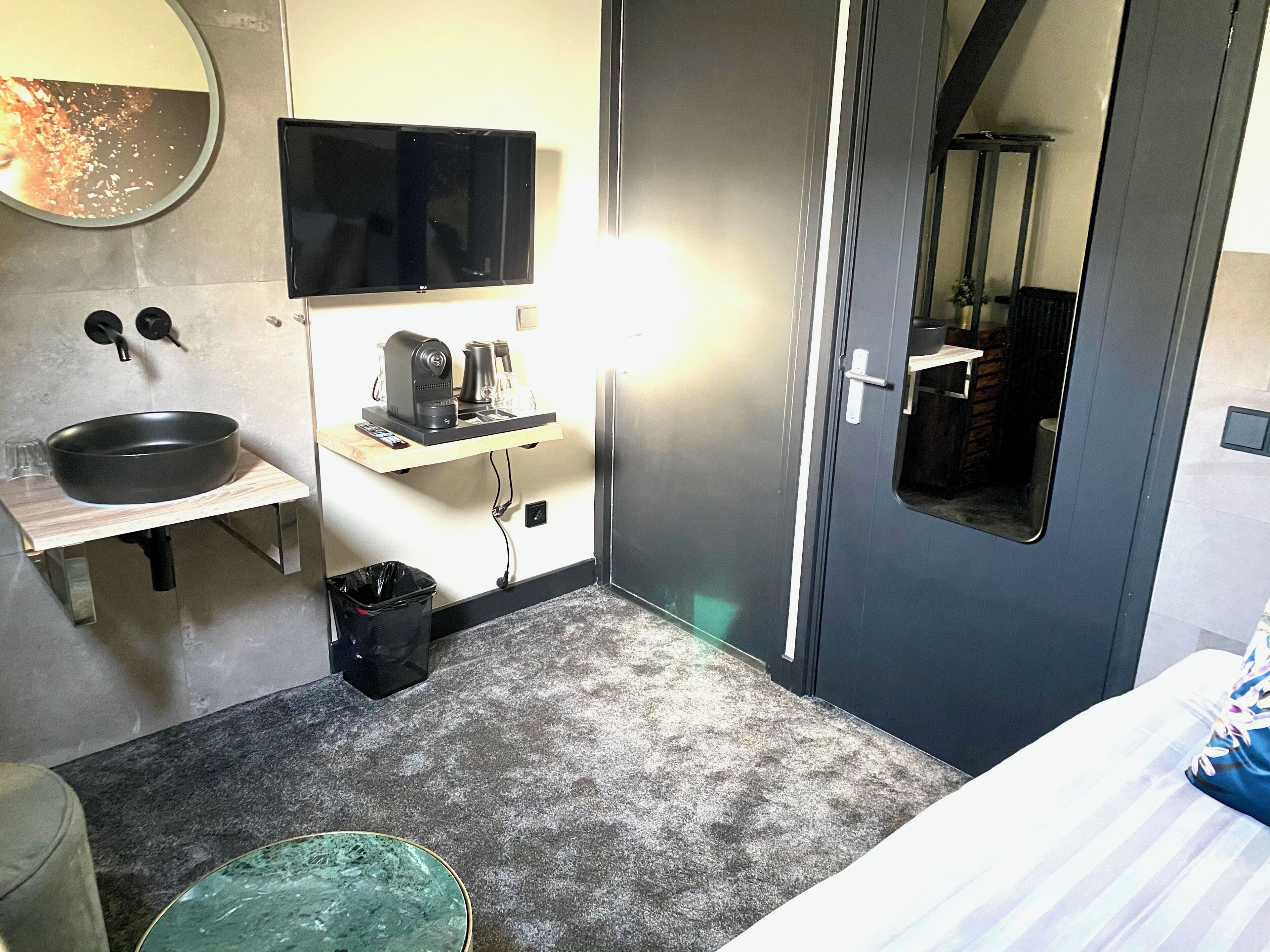 Pieni hotellihuone, jossa on pesuallas, peili, televisio ja pieni kahvinkeitin.