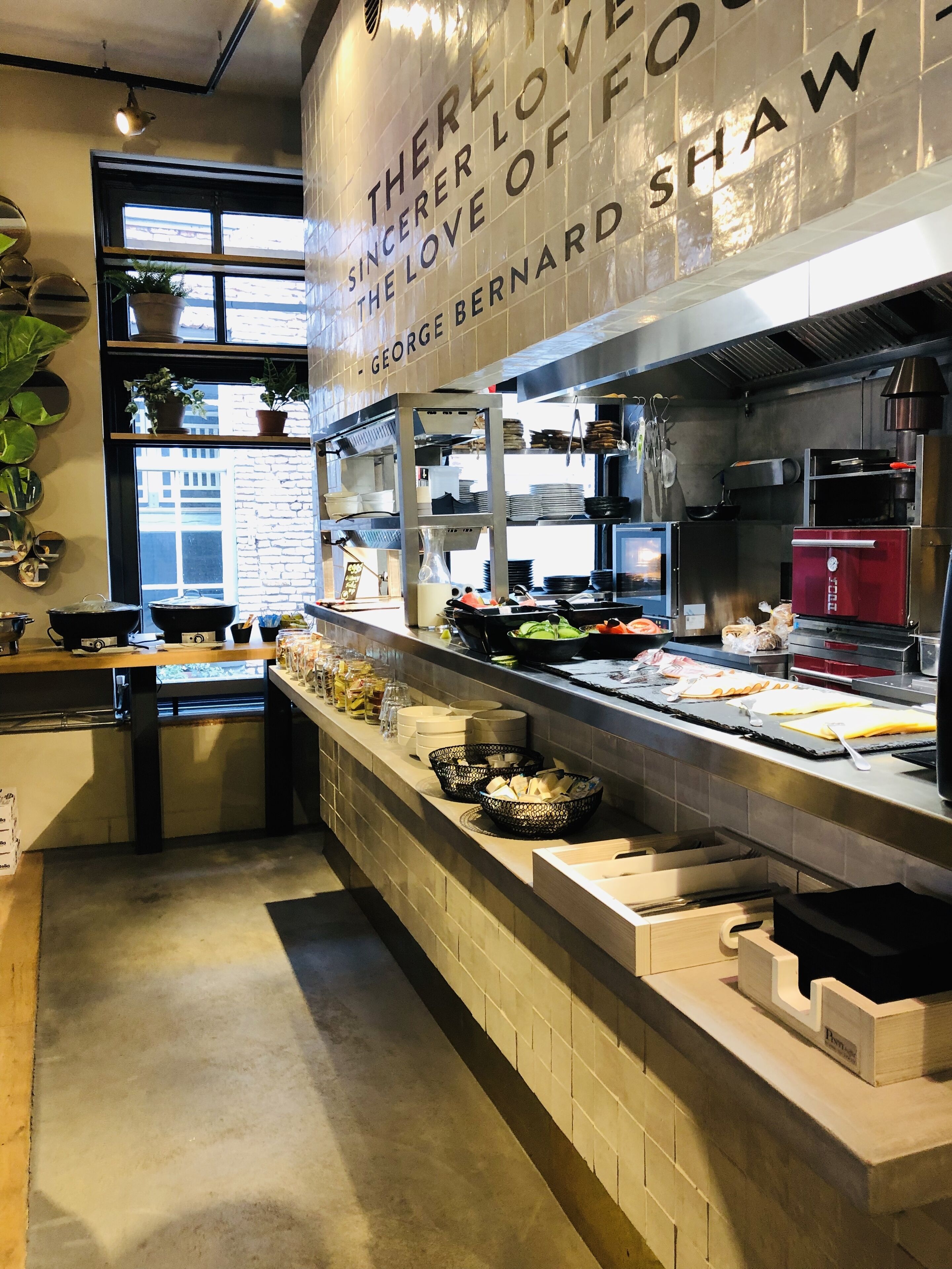 Eine Küche mit einer Edelstahl-Arbeitsfläche, verschiedenen Kochutensilien und einem Schild mit der Aufschrift 'THERE IS A LOVE FOR FOOD - GEORGE BERNARD SHAW'.