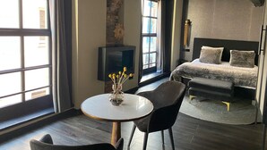 Una habitación de hotel con cama, televisión, mesa y sillas, y ventanas amplias.