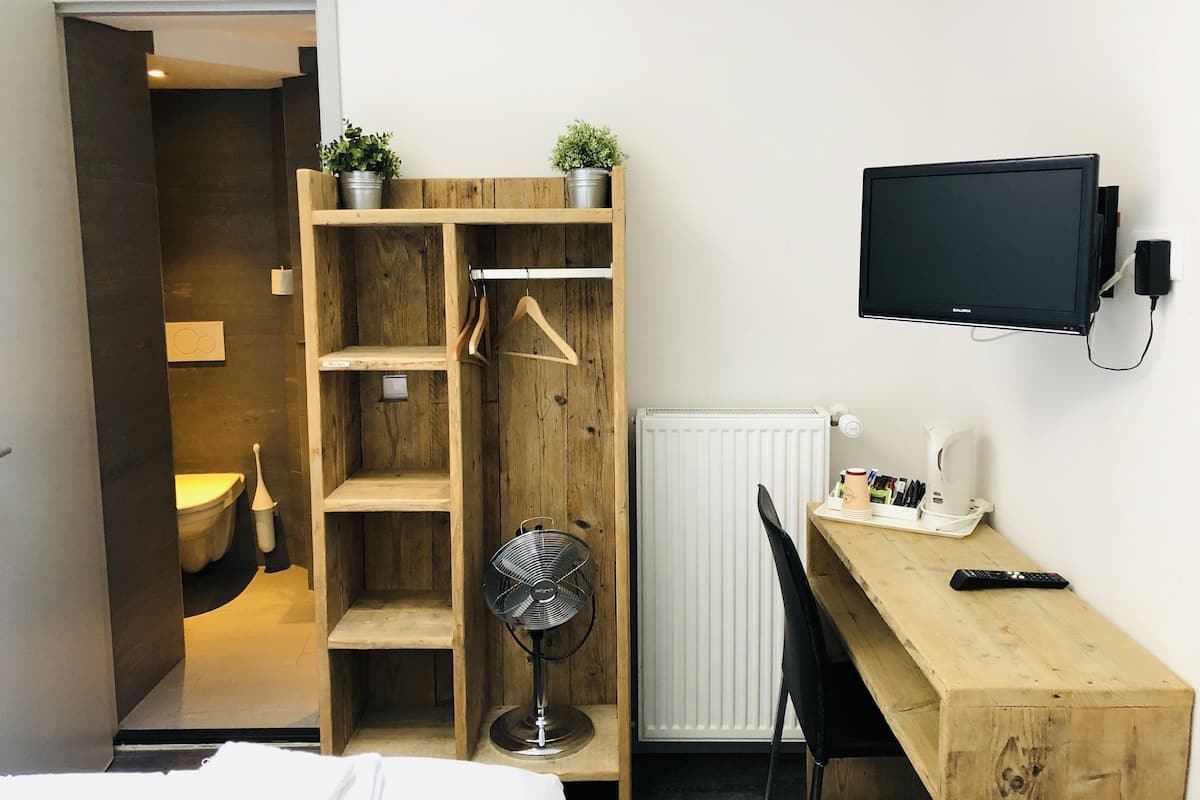 Une pièce comprenant une armoire en bois, un bureau avec une télécommande, un radiateur et un téléviseur fixé au mur.