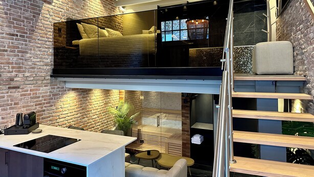 Una habitación moderna estilo loft con cama en el altillo, zona de comedor y cocina integrada, y una escalera.