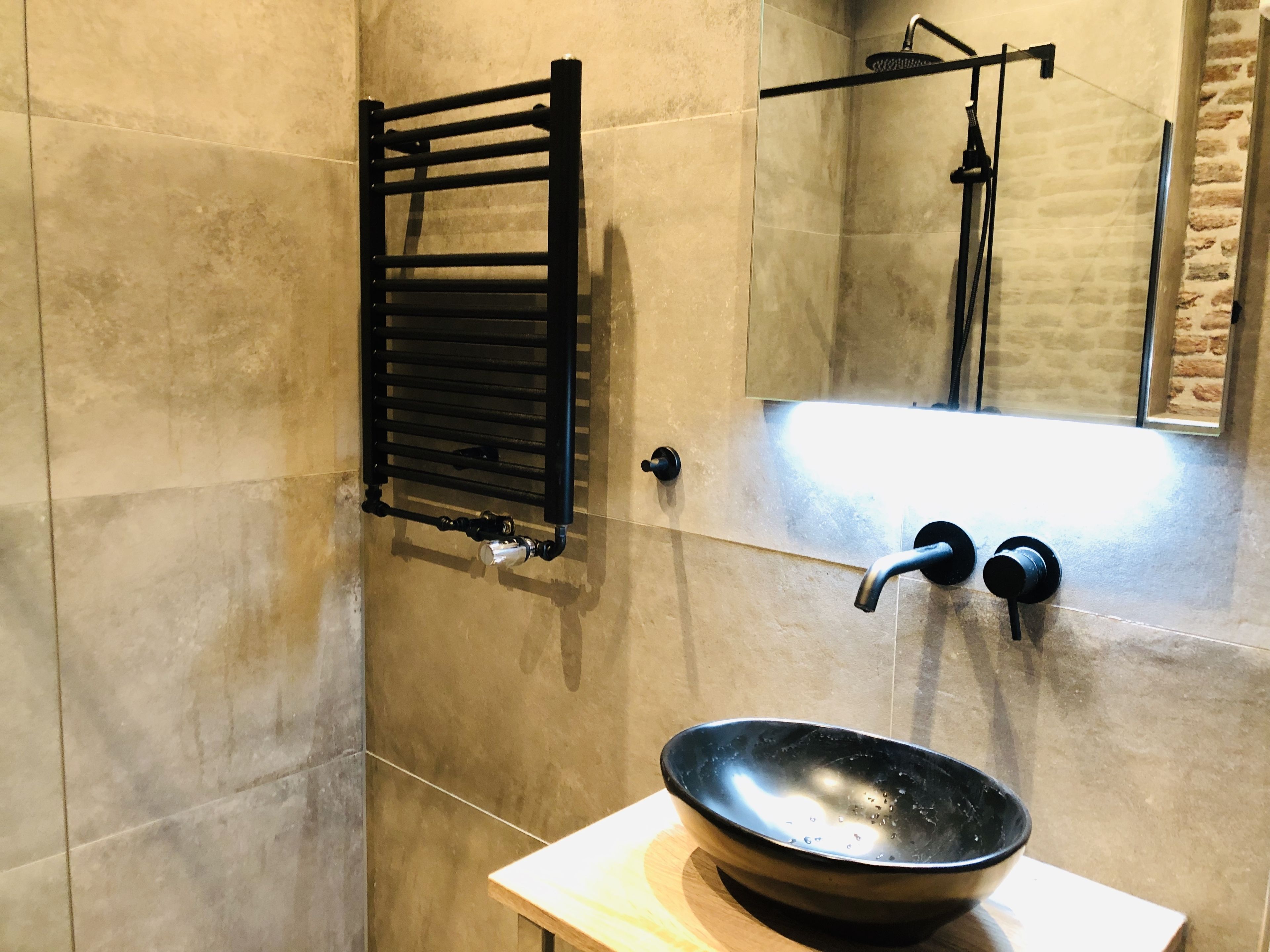 A bathroom with a black towel rack, a sink with a black basin, and a shower area with a glass door.