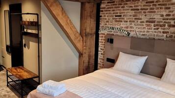 A bedroom with a bed, a wooden bench, a coat rack, and a brick wall.