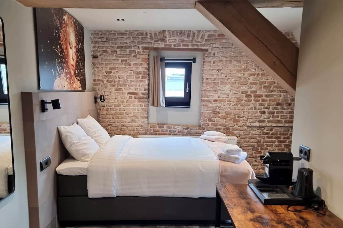 Une chambre avec un lit, une petite fenêtre, une machine à café et une table en bois.