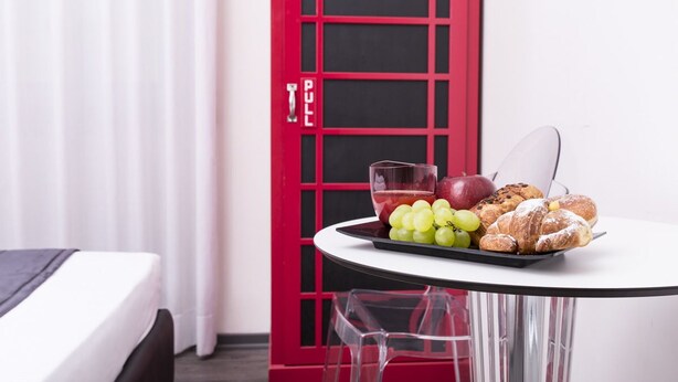 A hotel room with a bed, a dining table with a fruit and pastry tray, a red door, and a white curtain. - Il Giglio Rosso - B&B (Florence)