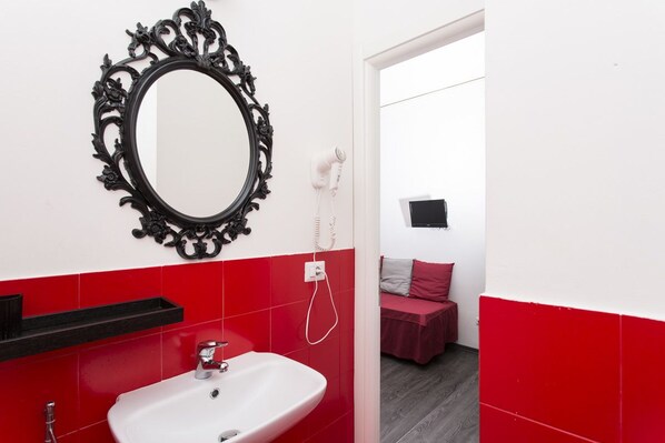 A bathroom with a white sink, red tiles, a black ornate mirror, and a red bench in the background.