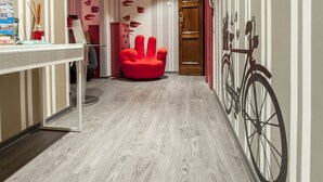 A hallway with a wooden floor, a red chair, a bicycle wall art, and a wooden door. - Il Giglio Rosso - B&B (Florence)