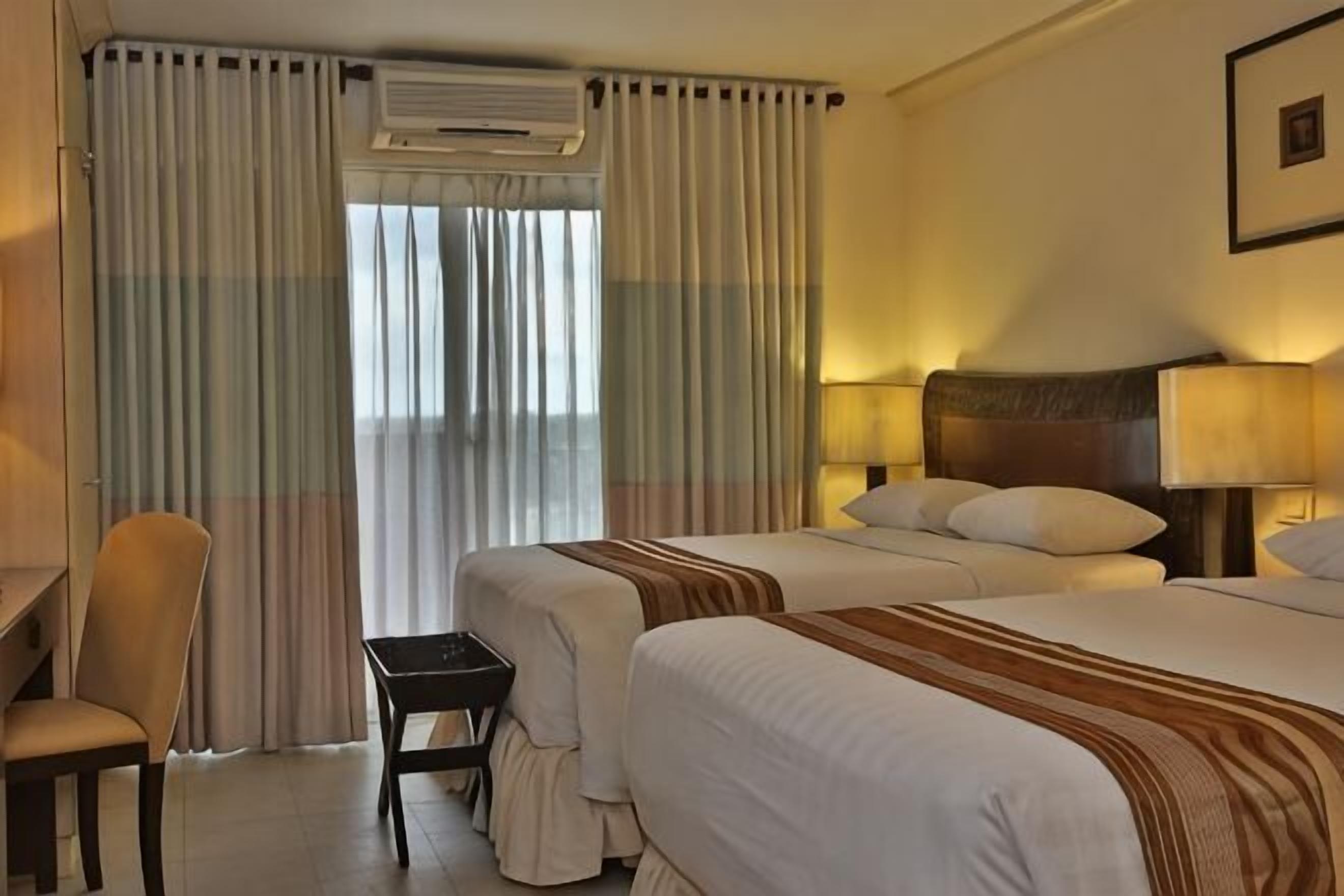 A hotel room with two beds, a desk, a chair, and a window with curtains.
