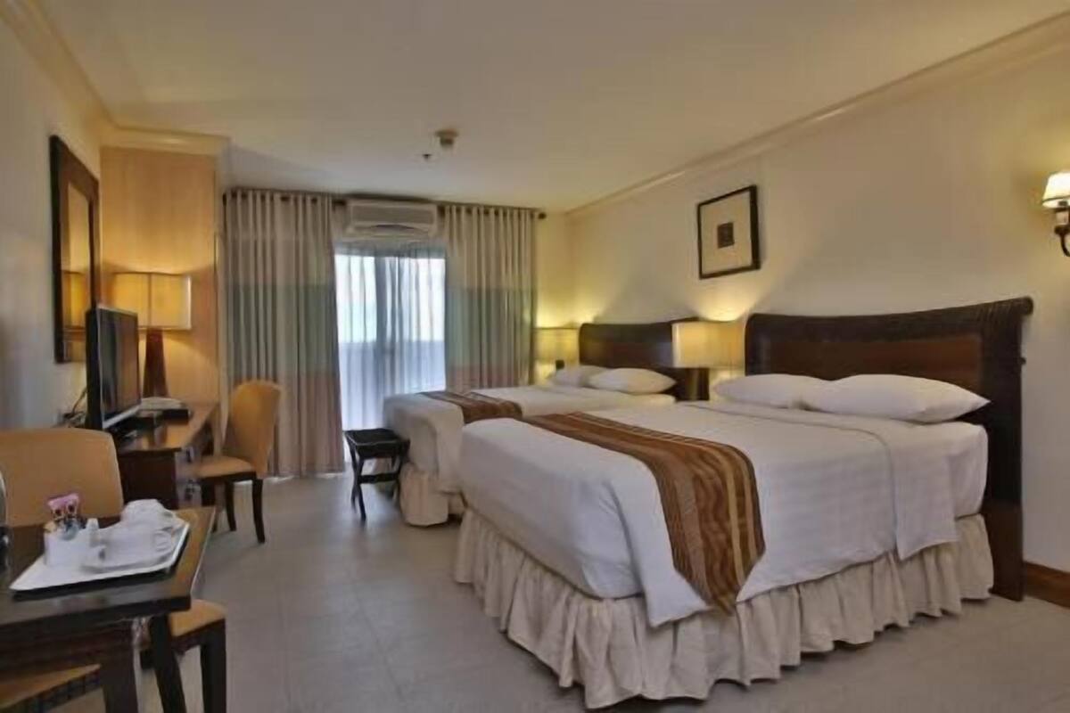 Habitación de hotel con dos camas, un escritorio, una silla, televisión y ventana con cortinas.