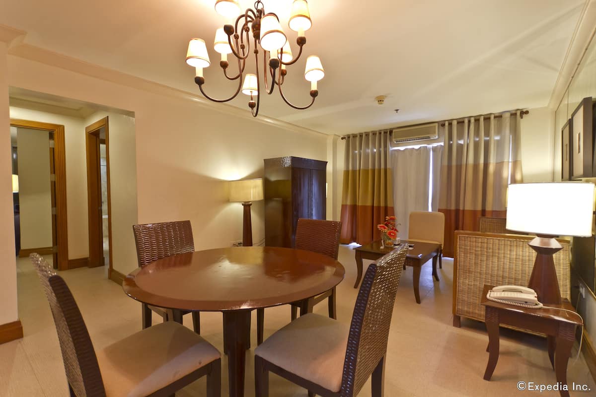 A hotel dining area with a round table, chairs, a chandelier, and a television.
