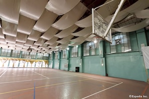 En basketplan inomhus med högt tak, gröna väggar och en basketkorg.