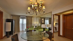 A hotel room with a round glass table, patterned chairs, a chandelier, a sofa, and a bed. - Crown Regency Suites & Residences - Mactan (Lapu-Lapu)