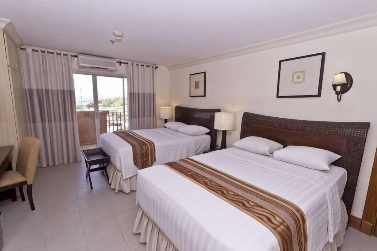 A hotel room with two beds, a chair, a desk, and a balcony.