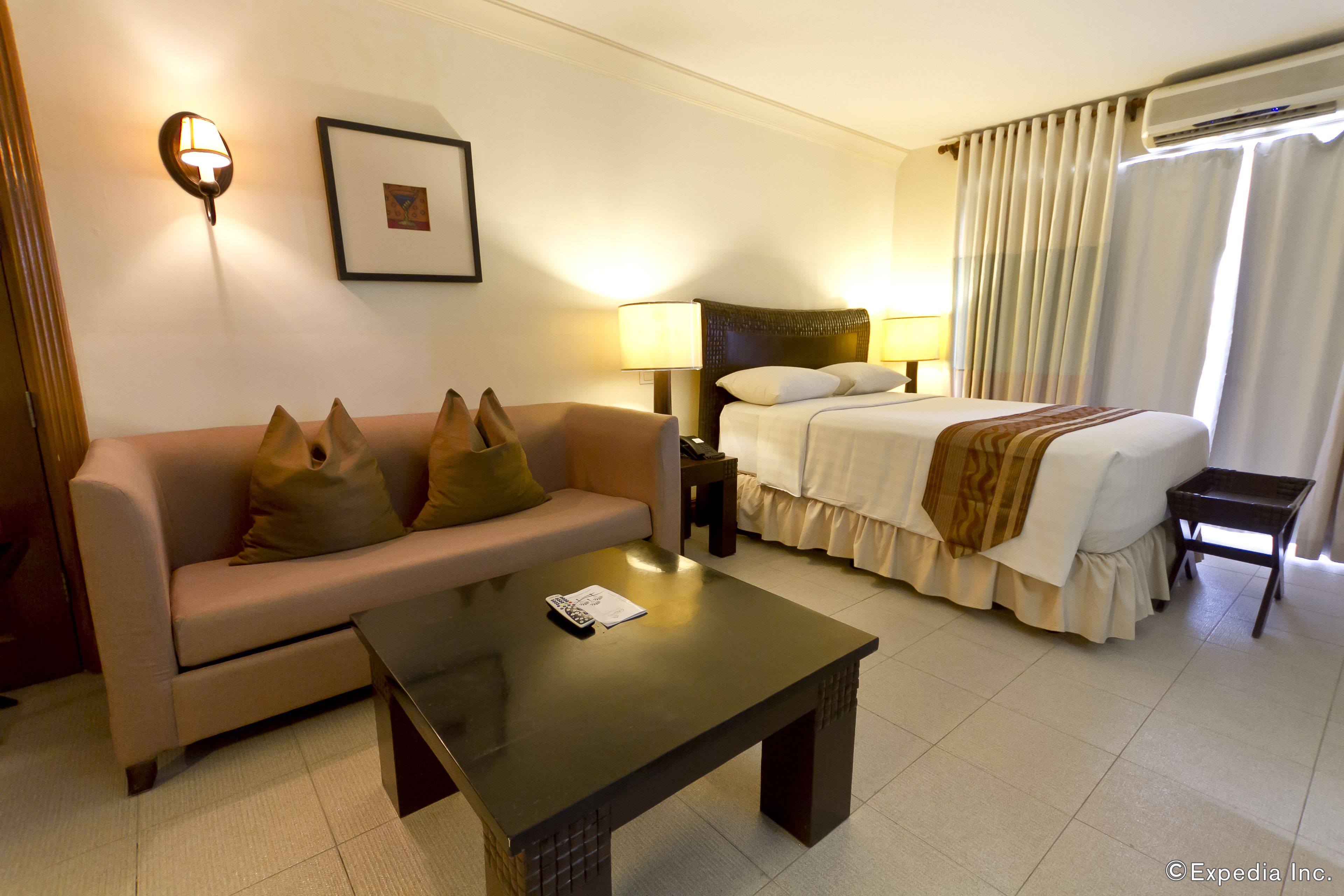 A hotel room with a sofa, a bed, a bedside table, and a small table.