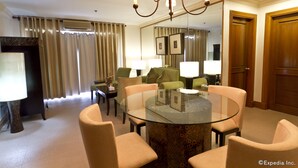 A hotel room with a round glass table surrounded by four chairs, a chandelier, a large mirror, and a television on a stand. - Crown Regency Suites & Residences - Mactan (Lapu-Lapu)
