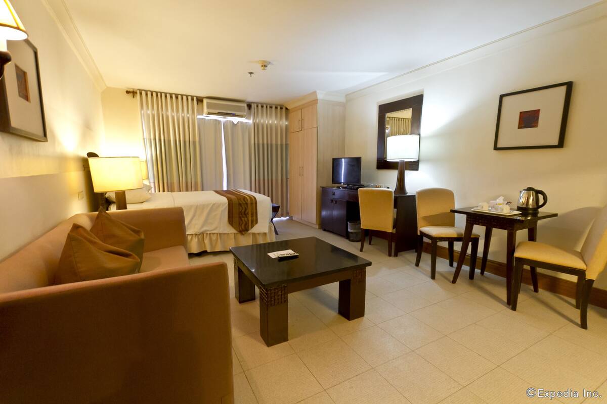 A hotel room with a bed, a sofa, a coffee table, a TV, a desk, and a chair.
