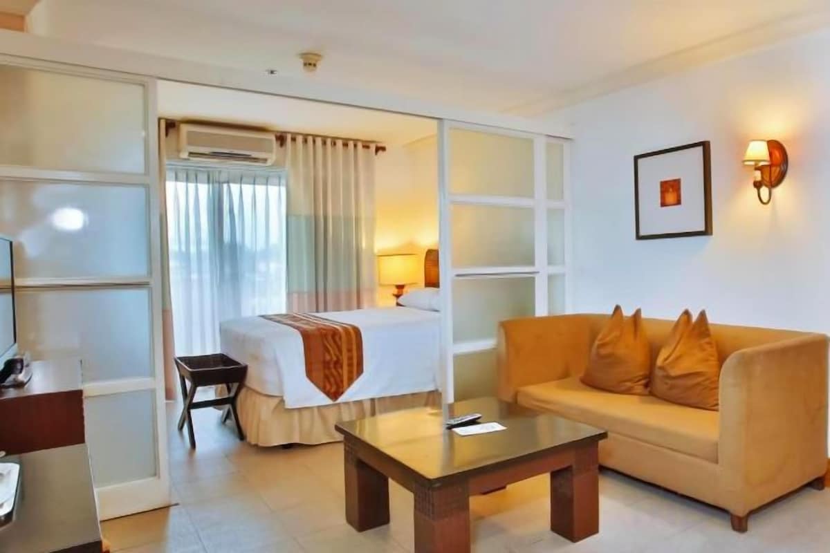 Habitación de hotel con cama, sofá, mesa de centro, escritorio y una silla.
